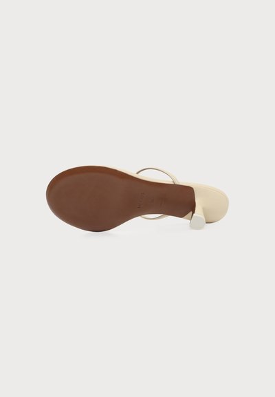 Sandale beige unique vue de la semelle, affichant un dessous marron lisse, un bout ouvert et un talon carré sur fond blanc.