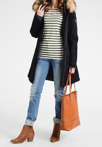 Navy parka with fur-trimmed hood, striped shirt, blue jeans, tan ankle boots, and brown tote bag. Features button closures and rolled cuffs.