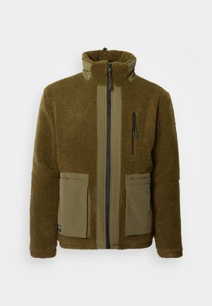 Olajzöld polárdzseki magas gallérral, cipzárral, két elülső zsebbel, valamint eltérő szövetpanelek a mellrészen és az ujjakon.