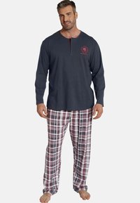 Men's pajama set featuring a dark gray henley top with a red logo, and plaid pants in red, white, and navy. Cotton fabric, relaxed fit.