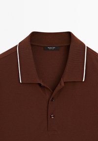 Polo marron avec une bordure blanche au col, deux boutons sur la patte de boutonnage, et une étiquette Massimo Dutti visible à l'intérieur du col.