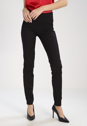 Zwarte slim-fit broek van rekbaar materiaal, met een gladde textuur, een middenhoogte taille en een minimalistisch ontwerp. Gecombineerd met zwarte hakken.