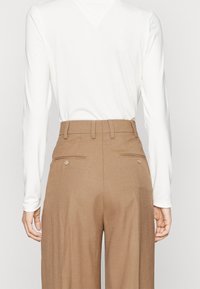 White long-sleeve top and high-waisted brown trousers with a smooth texture, featuring two back pockets with buttons and belt loops.