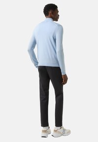 Lichtblauwe gebreide trui met een hoge kraag, gecombineerd met een donkere broek. Het model draagt witte sneakers met beige accenten.