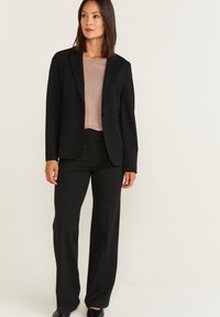 Zwart op maat gemaakt pak met een blazer met één knoop en rechte broek. Draag het over een zacht beige top, wat zorgt voor een professionele maar toch klassieke uitstraling.