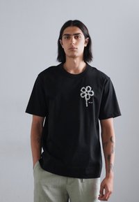 Sort bomulds t-shirt med et hvidt blomstermotiv på brystet, korte ærmer og en afslappet pasform. Glat tekstur med en rund halsudskæring.