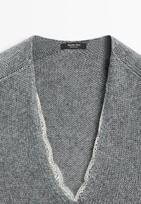 Grijze gebreide trui met een V-hals, voorzien van een delicaat kanten randje. De textuur is zacht en benadrukt het breipatroon overal.