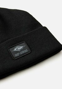 Gorro de punto negro con un borde doblado y un parche rectangular negro con un logo gris que dice "RIP CURL". Textura suave, diseño minimalista.