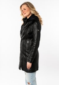 Zwarte leren jas met een ritssluiting, gevoerde capuchon en twee verticale ritszakken op de borst. Heeft stikseldetails en gedempte hardware accenten.