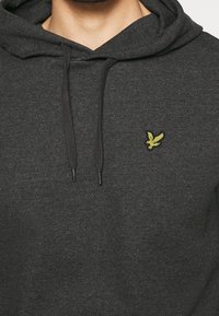 Hoodie grigio scuro realizzato in tessuto morbido, con una tasca a marsupio frontale, coulisse regolabili e un piccolo logo ricamato giallo sul petto.