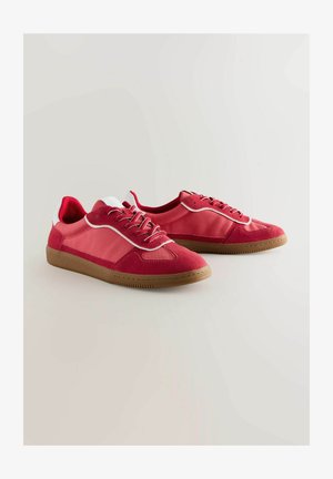 Červené atletické boty s kombinací semiše a syntetických materiálů. Jsou vybaveny gumovou podrážkou, šněrováním a kontrastními bílými akcenty.