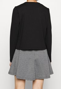 Černý dlouhý rukáv svetr s crop designem, který je zkombinován s rozšířenou sukni v černobílém kostkovaném vzoru. Hladká tkanina a jednoduché detaily šití.
