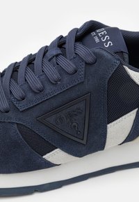 Sneaker blu navy con materiali in suede e mesh, logo triangolare, lacci tonali e accenti argentati a contrasto sui lati.