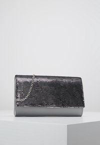 Stříbrná peněženka s flitry na hladkém šedém podkladu, s řetízkem a obdélníkovým tvarem. Texturovaný, lesklý povrch.