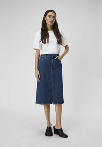 Jupe midi en denim avec fente à l'avant, design à cinq poches et taille haute. Associée à un haut blanc à manches courtes et des mules noires.