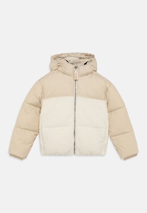 Doudoune beige avec un panneau en polaire blanche duveteuse, une capuche et une fermeture éclair à l'avant. Design matelassé avec des poignets élastiques et un détail en étiquette en bois.