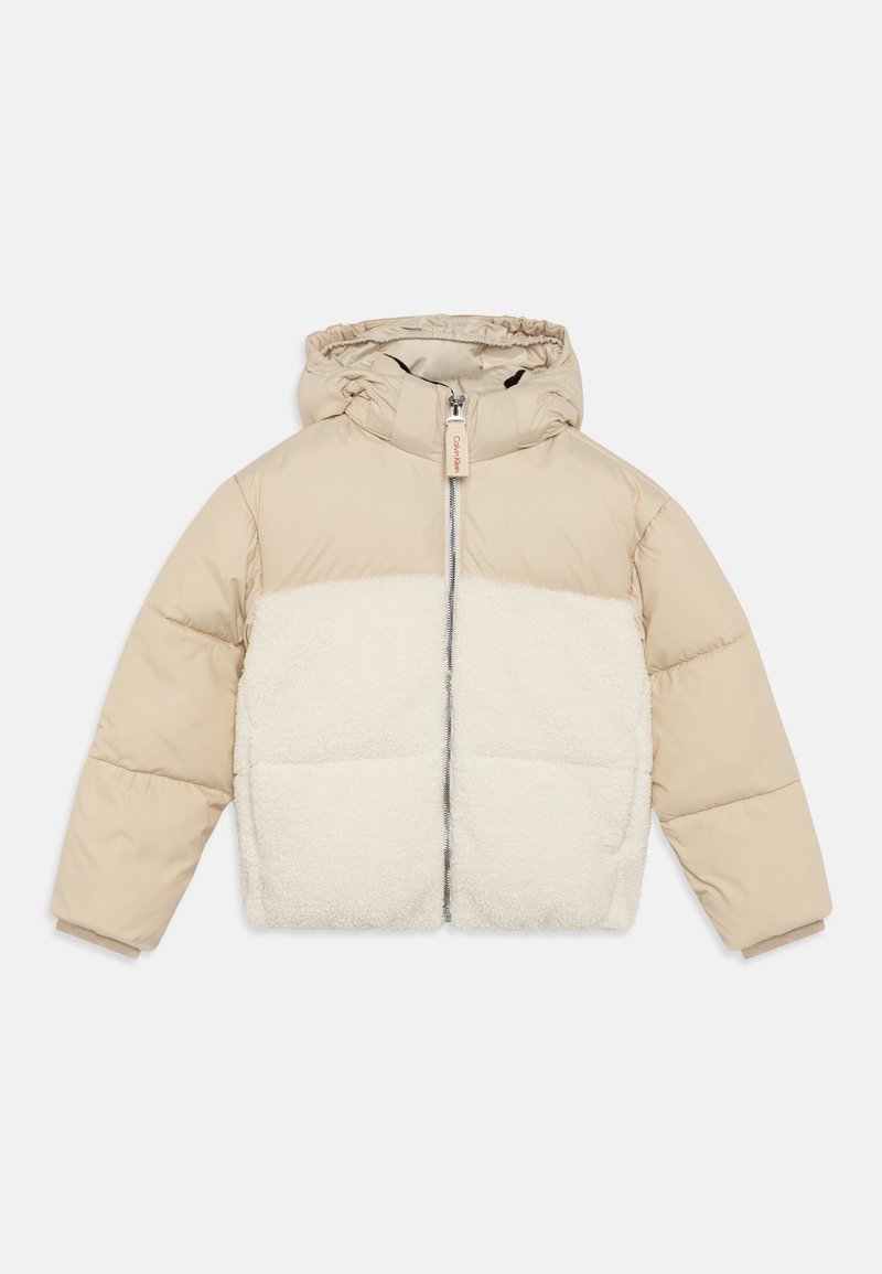 Beige puffjakke med en fluffy hvit fleecepanel, hette og frontglidelås. Kviltet design med elastiske mansjetter og en tre-tag detalj.