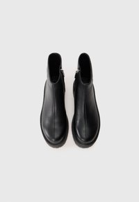 Une paire de bottes de cheville en cuir noir, à bouts ronds et avec des fermetures éclair sur les côtés, vues de dessus sur un fond blanc uni.
