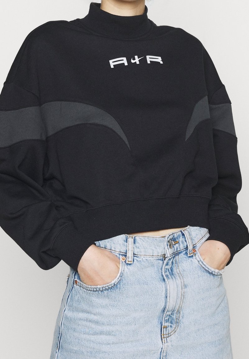 Svart kort sweatshirt med hög krage, som har kontrasterande grå ränder och vit logotyptext. Matchad med ljusblå denimshorts.