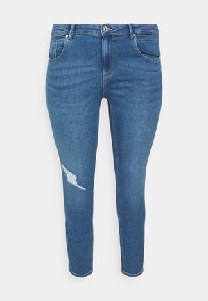 Jeans ajustados de mezclilla azul con una cintura de altura media, con una rodilla desgastada y un diseño clásico de cinco bolsillos. Textura suave con un leve desgastado.