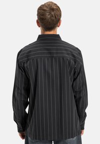 Zwarte lange mouw shirt met verticale witte strepen, knopenmanchetten en een kraag; heeft een losse, ontspannen pasvorm en een zachte katoentextuur.