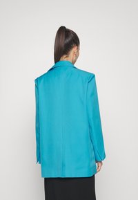 Tyrkysový blazer s přizpůsobeným střihem, s jedním zadním ventilem a špičatými klopami, vyrobený z hladké, lehké látky. Zobrazeno ze zadní strany.