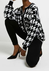 Svartvit hundtandsmönstrad cardigan med en fluffig textur och grå kant; ihop med svarta leggings och spetsskor med slingback.