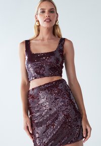 Bordeaux twee-delige outfit bestaande uit een bedekte croptop met vierkante halslijn en een bijpassende mini-jurk met pailletten. Glanzende textuur overal.