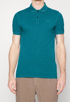 Polo tee bleu-vert en coton doux, avec un col classique, une patte de boutonnage à deux boutons et un détail logo subtil sur la poitrine. Manches courtes.