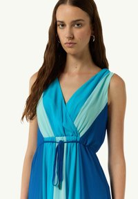 Ärmelloses V-Ausschnitt-Kleid mit einem Farbverlauf in Blau, geraffter Taille und einer Bindeeinheit. Weicher, fließender Stoff mit einer eleganten Silhouette.