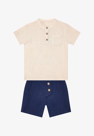 Beige overhemd met korte mouwen, drie knopen en borstzak, gecombineerd met marineblauwe shorts met twee knopen aan de voorkant.