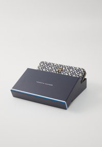Tommy Hilfiger wallet in a cream and navy geometric pattern. Zipper closure, metal logo accent. Packaged in a navy box with logo.