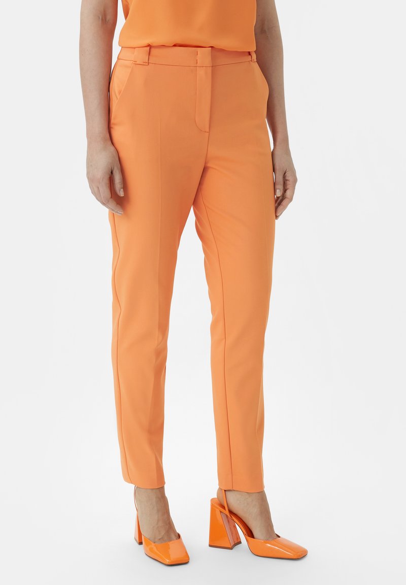 Orange tailored trousers with a slim fit, featuring a flat front and side pockets, paired with shin-high orange block-heeled shoes.