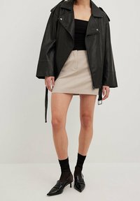 Černá koženka s oversized střihem, matnou texturou a širokým límcem. Spárována s béžovou mini sukní a černými špičatými lodičkami.