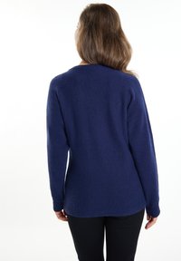 Marineblau gestrickter Pullover mit langen Ärmeln, rundem Ausschnitt und strukturierter Stoff. Der Saum ist hinten leicht länger.