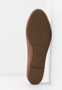 Semelle d'une chaussure marron Michael Kors montrant un motif de bande de roulement avec des logos "MK" répétés et un logo circulaire près de la voûte plantaire.