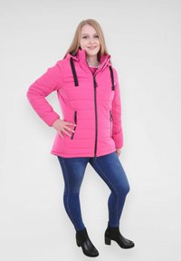 Roze pufferjack met een rits aan de voorkant, verstelbare capuchon, zwarte accenten en twee zijzakken, gecombineerd met donkere spijkerbroeken en zwarte enkelboots.