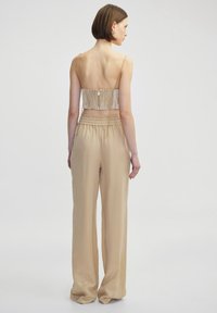 Beige wide-leg pants with an elastic waist, paired with a sheer, patterned back top featuring thin straps and a fitted design.