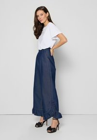Witte korte mouwen t-shirt gecombineerd met high-waisted donkerblauwe denimbroek met ruches aan de onderkant, gedragen met zwarte hoge hakken sandalen.