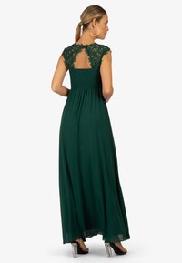 Langes grünes Kleid mit Spitzenkurzärmeln und gesmoktem Oberteil. Fließender Stoff mit einem Schlüsselloch-Ausschnitt im Rücken und bequemer Passform.