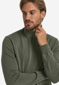 Grüner Rollkragenpullover aus weichem Stoff, mit gerippten Bündchen und Saum, in schmaler Passform und glatter Textur.