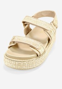Sandalias de cuña beige con tiras tejidas texturizadas, hebilla ajustable y una base de plataforma gruesa. La suela interior suave contrasta con la parte superior.