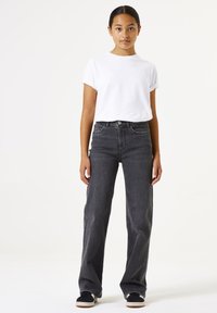 Jeans negros de talle alto con corte recto, combinados con una camiseta blanca de manga corta. El conjunto presenta diseños simples y clásicos.