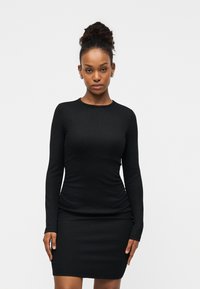 Μαύρο φόρεμα με μακριά μανίκια και εφαρμοστή σιλουέτα, με ριμπ υφή και στρογγυλή λαιμόκοψη. Μινιμαλιστικός σχεδιασμός χωρίς ορατά μοτίβα ή διακοσμητικά στοιχεία.