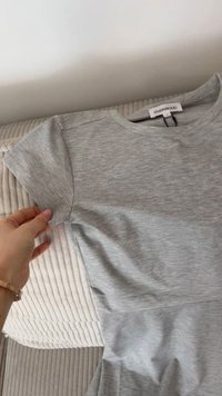 Szara koszulka z krótkim rękawem, wykonana z miękkiego materiału, z okrągłym dekoltem i lekko dopasowanym krojem. Metka widoczna z tyłu.