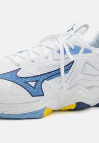 Zapatilla deportiva blanca con un detalle de diseño azul, parte superior texturizada y una suela multicolor con acentos en azul, amarillo y marino.