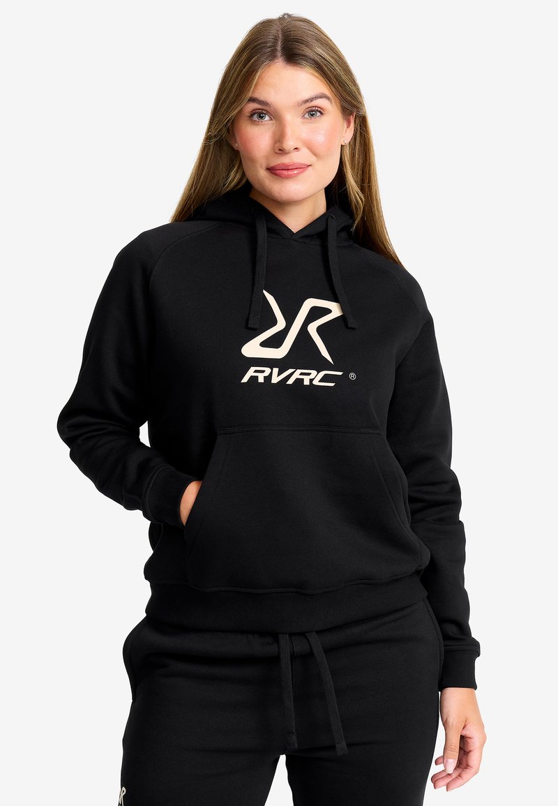 Svart hoodie med en framficka, dragsko huva och stor beige RVRC-logotyp på bröstet; ihop med matchande svarta byxor.