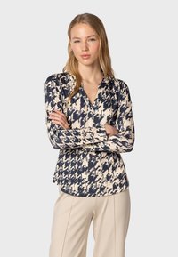 Blouse à manches longues avec un motif abstrait bleu marine et crème. Fabriqué en tissu léger avec un col et une coupe décontractée.