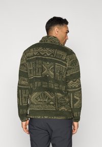 Green fleece sweater featuring a textured, patterned design with geometric shapes and subtle tonal variations. High collar and relaxed fit.