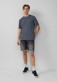 Graues Rundhals-T-Shirt kombiniert mit dunklen Denim-Shorts, hochgekrempelten Säumen und schwarzen Sneakers, ergänzt durch weiß gestreifte Socken.